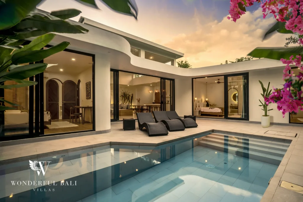 The private pool and sun loungers on the terrace framed by the villa's sliding glass doors and tropical plants under a sunset sky at a 3-bedroom villa in Bingin, Uluwatu, Bali