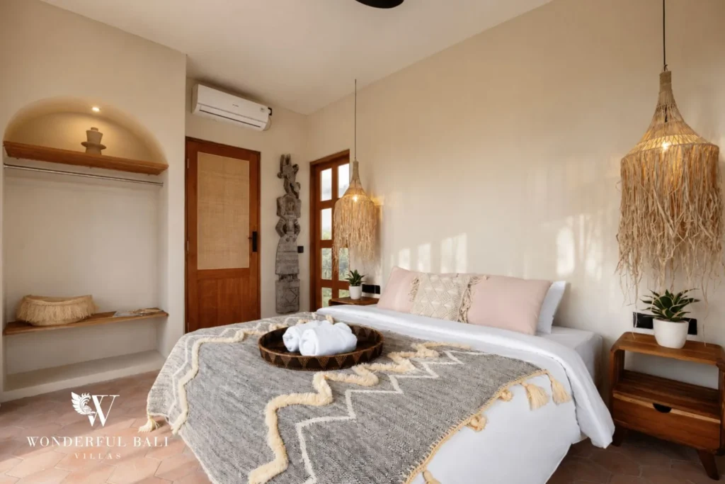 A serene queen bedroom with tasseled throw, arched niche and rattan pendant lamps at a 3-bedroom villa in Pererenan, Bali