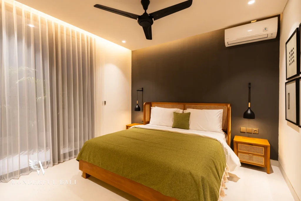 A cozy bedroom with a cane headboard, olive-green bedspread, dark feature wall, rattan bedside tables and sheer curtains at a 5-bedroom villa in Batu Bolong, Canggu, Bali