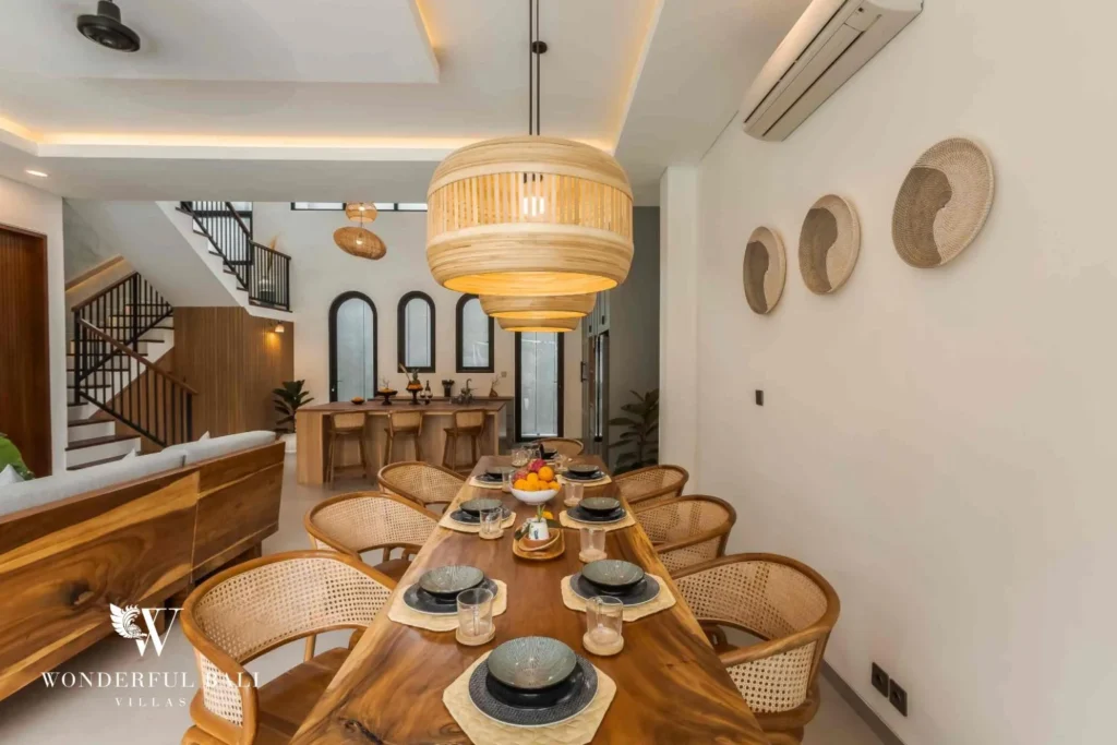 A long live-edge dining table with rattan chairs and woven wall decor leading toward the kitchen and staircase at a 4-bedroom villa in Pererenan, Bali
