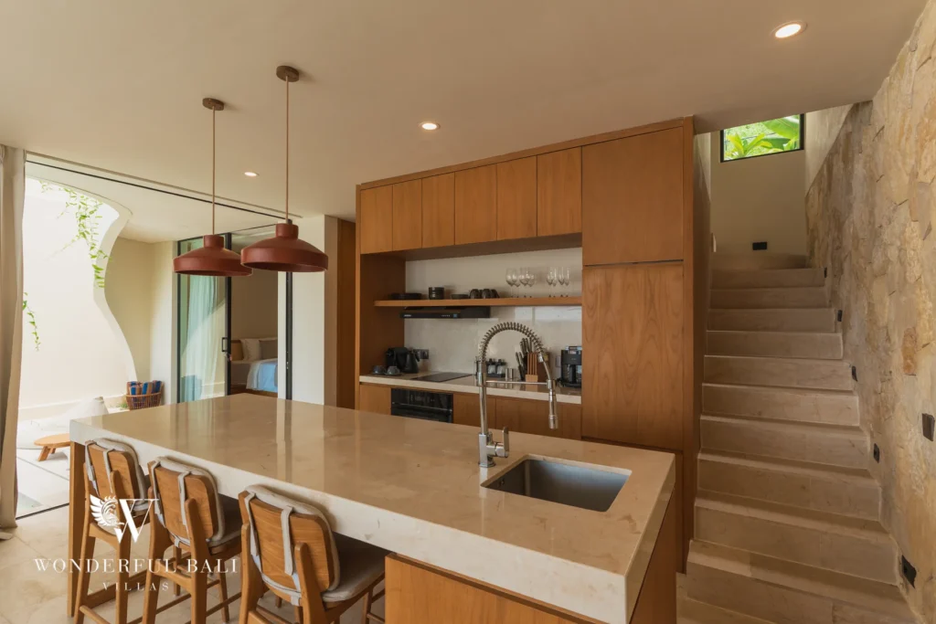 A kitchen with a stone island, timber cabinetry, bar stools and a staircase leading upstairs at a 3-bedroom villa in Bingin, Uluwatu, Bali