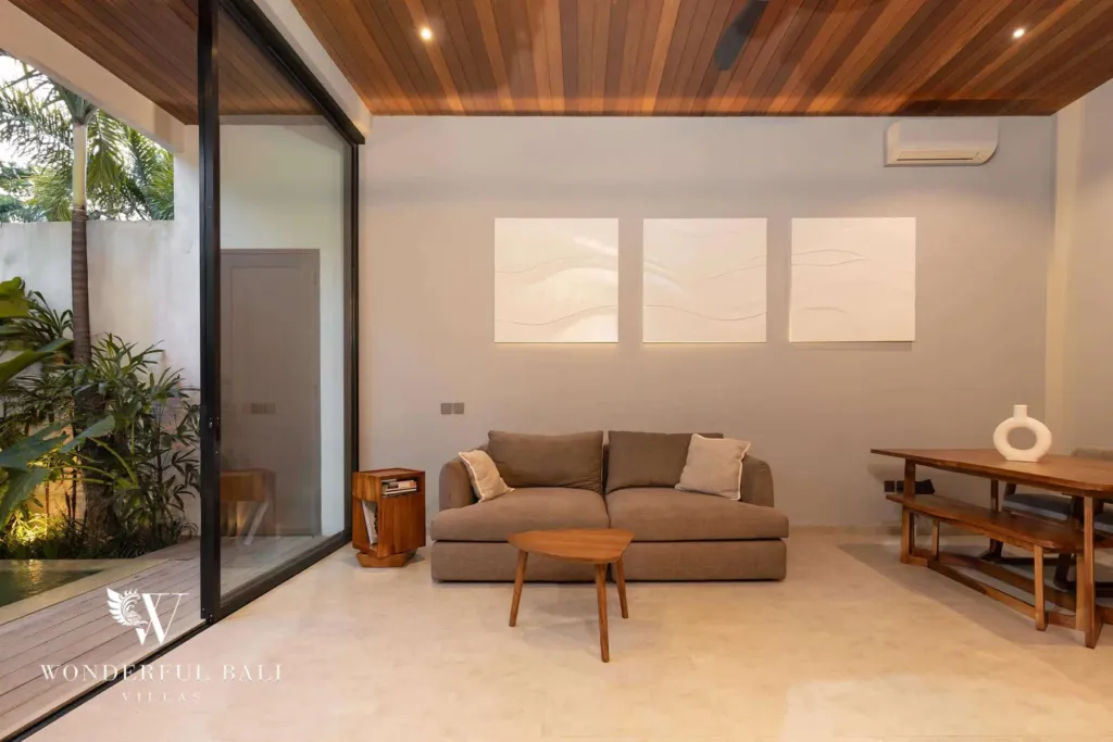 2BR villa for rent in Pererenan — living room, a living and dining room in the evening with a brown sofa, wood dining set and sliding doors framing a lantern-lit pool deck at a 2-bedroom villa