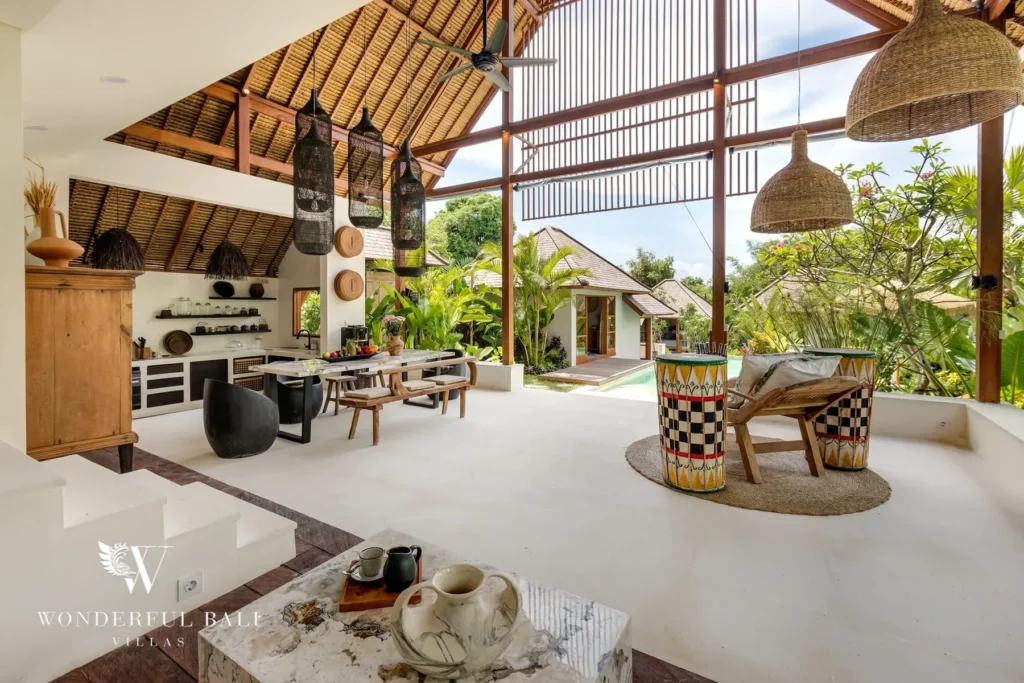 An open-sided living and dining pavilion with high timber ceilings, woven pendant lamps and patterned drum stools opens to the pool and garden at a 4-bedroom villa in Canggu, Bali
