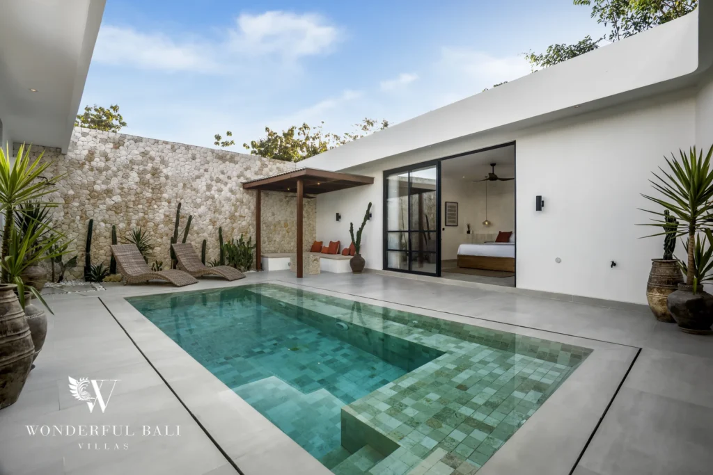 A private pool with sun loungers, a shaded seating nook and a stone wall under a blue sky beside a bedroom at a 3-bedroom villa in Bingin, Uluwatu, Bali