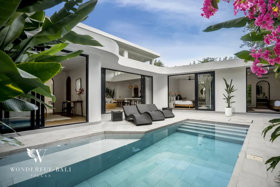 The private pool, sun loungers and terrace wrapped by the villa's open sliding glass doors and lush foliage under a blue sky at a 3-bedroom villa in Bingin, Uluwatu, Bali