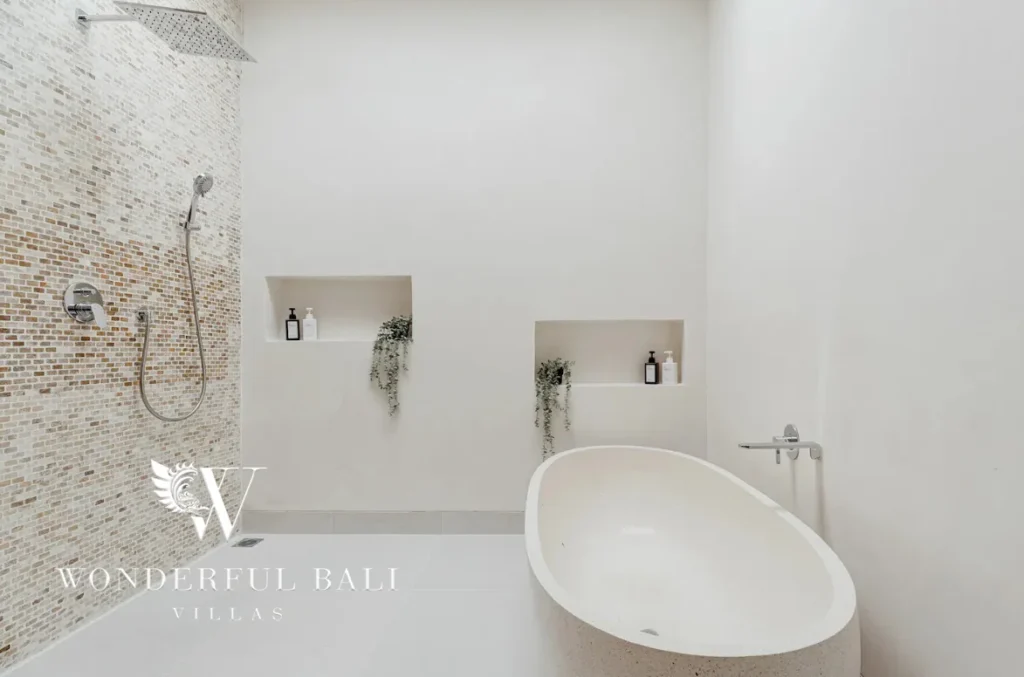 Minimalist bathroom with a freestanding oval stone tub, walk-in shower with mosaic tiling and recessed wall niches with plants at a 3-bedroom villa in Bingin, Uluwatu, Bali