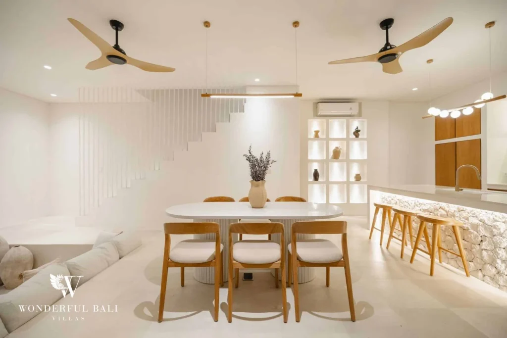 A round dining table with wooden chairs beneath ceiling fans, next to the kitchen bar and staircase, at a 2-bedroom villa in Bingin, Uluwatu, Bali
