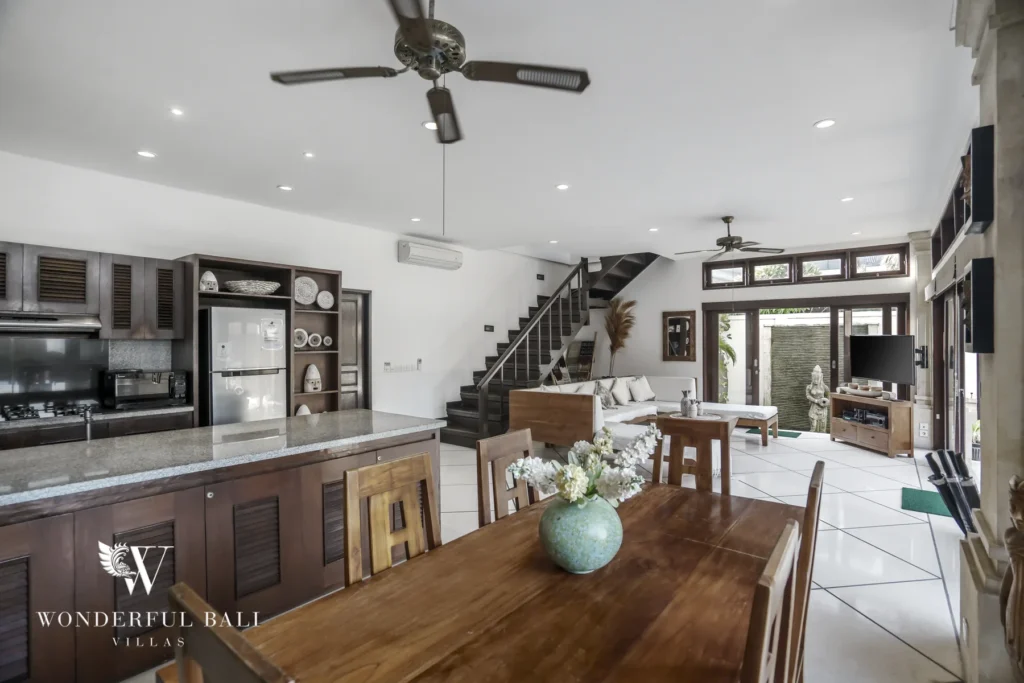 A combined kitchen, wooden dining table and living area with staircase opening to the terrace at a 4-bedroom villa in Seminyak, Bali