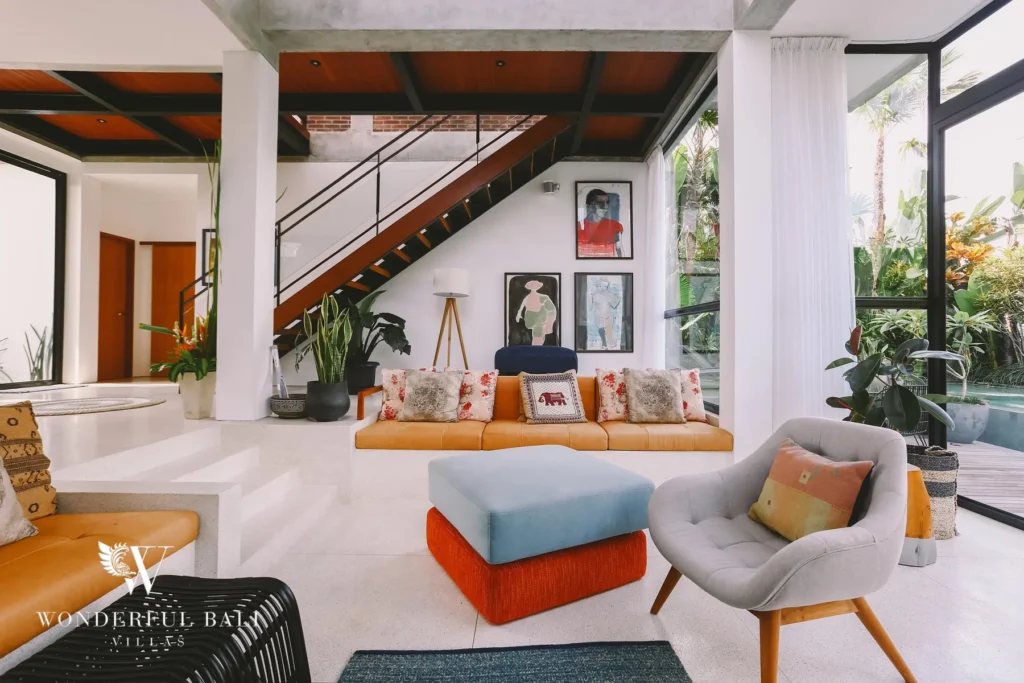 An open living area with a tan leather sofa, grey armchair and a floating timber staircase beneath a concrete ceiling at a 4-bedroom villa in Batu Bolong, Canggu, Bali