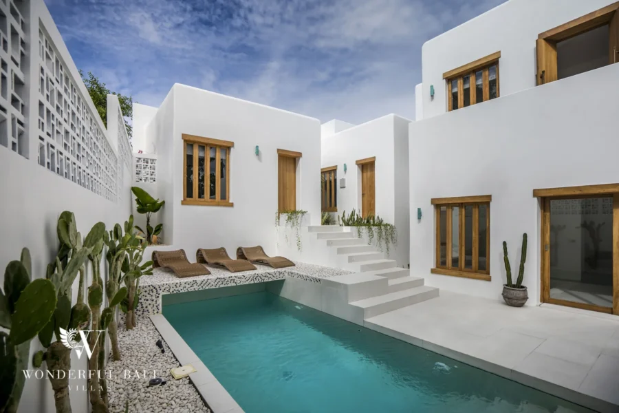 A private pool with cushioned sun loungers, potted cacti and white staircase set among bright whitewashed walls under a blue sky at a 3-bedroom villa in Bingin, Uluwatu, Bali