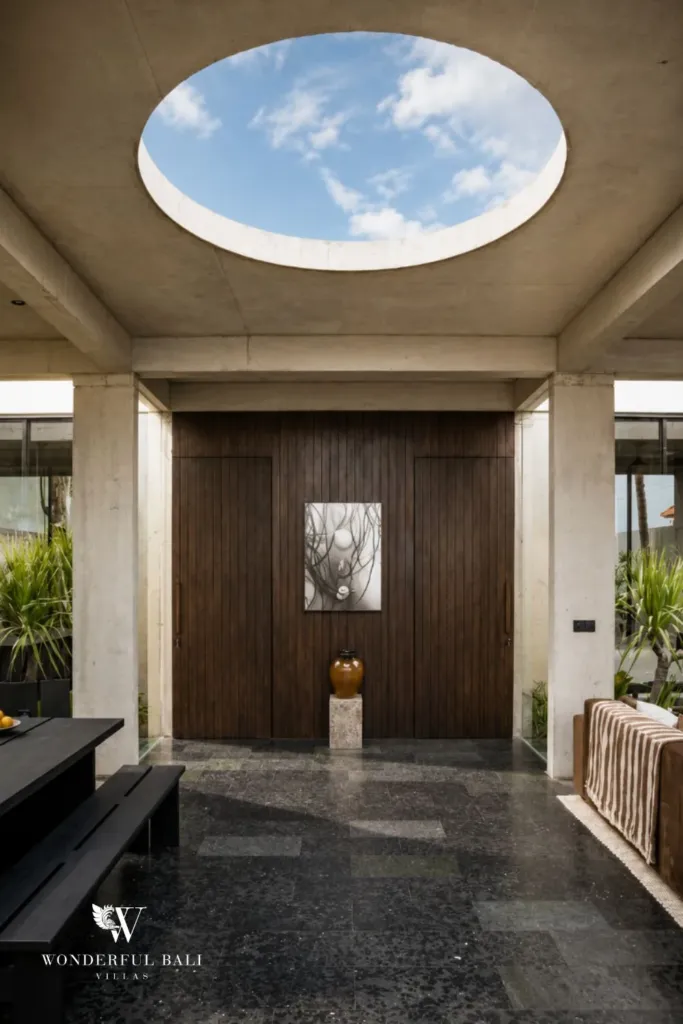 Central foyer beneath a round open skylight with timber doors, framed artwork and a ceramic vase on a stone plinth at a 2-bedroom villa in Seseh, Bali
