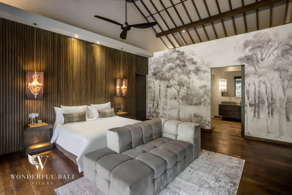 A spacious bedroom with a white bed, velvet bench, vaulted ceiling, forest-painted murals and an open ensuite vanity beyond at a 3-bedroom villa in Pererenan, Bali
