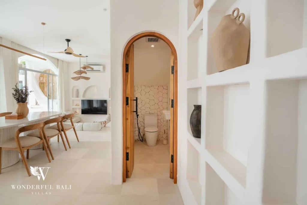 An arched wooden doorway leading from the dining area into a small stone-tiled toilet room, at a 2-bedroom villa in Bingin, Uluwatu, Bali