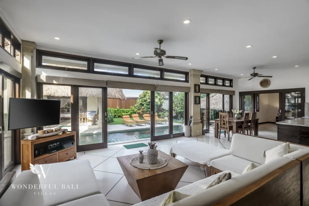 A spacious living room with white sofas and armchairs opening through glass doors to the pool and loungers at a 4-bedroom villa in Seminyak, Bali