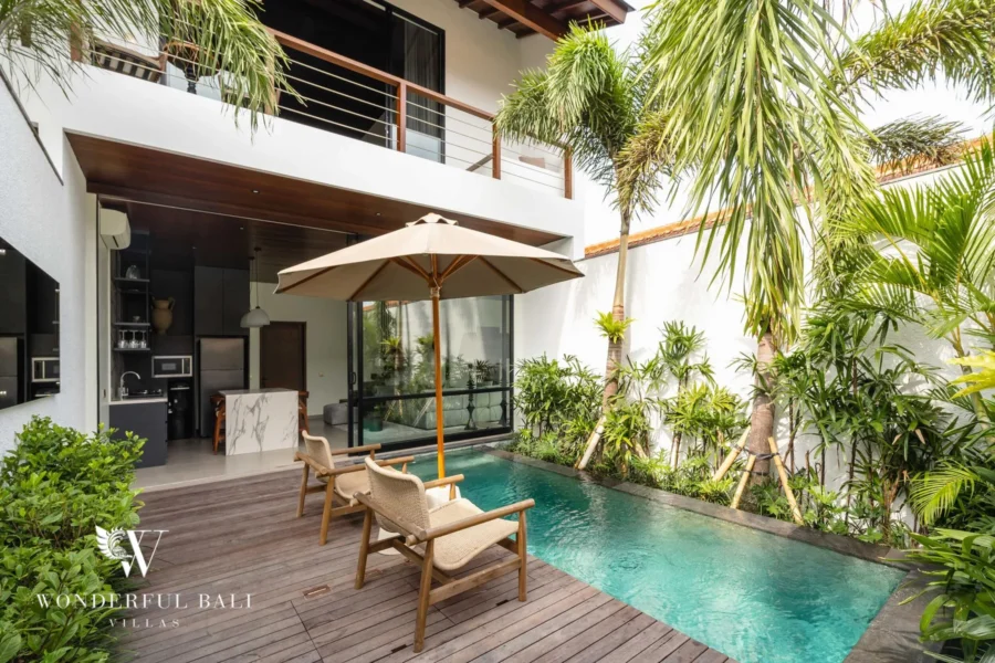 A courtyard pool with wooden deck, loungers and umbrella framed by palms below an upstairs balcony at a 2-bedroom villa in Canggu, Bali