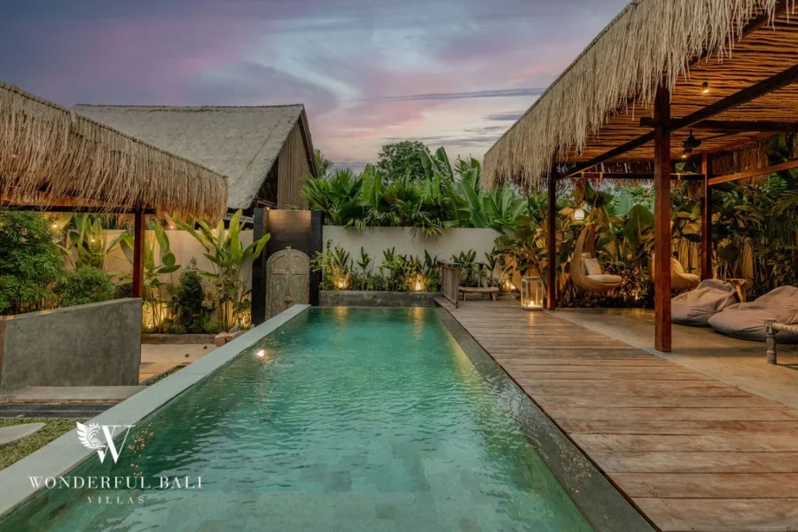 Private pool lit at dusk under a pink sky, framed by thatched pavilions with bean bags and lanterns on the deck at a 2-bedroom villa in Canggu, Bali