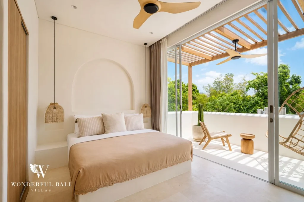 An upstairs bedroom with a beige-dressed bed opening through glass doors onto a private balcony over greenery, at a 2-bedroom villa in Bingin, Uluwatu, Bali