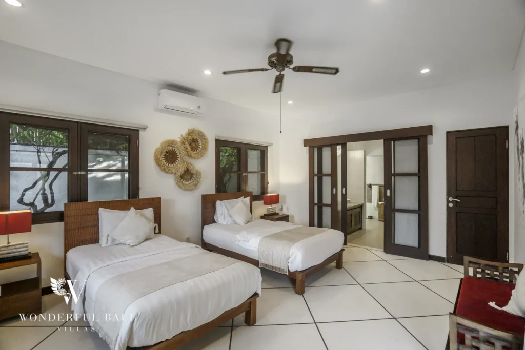 A twin-bed bedroom with woven headboards and wall baskets leading to an en-suite bathroom at a 4-bedroom villa in Seminyak, Bali