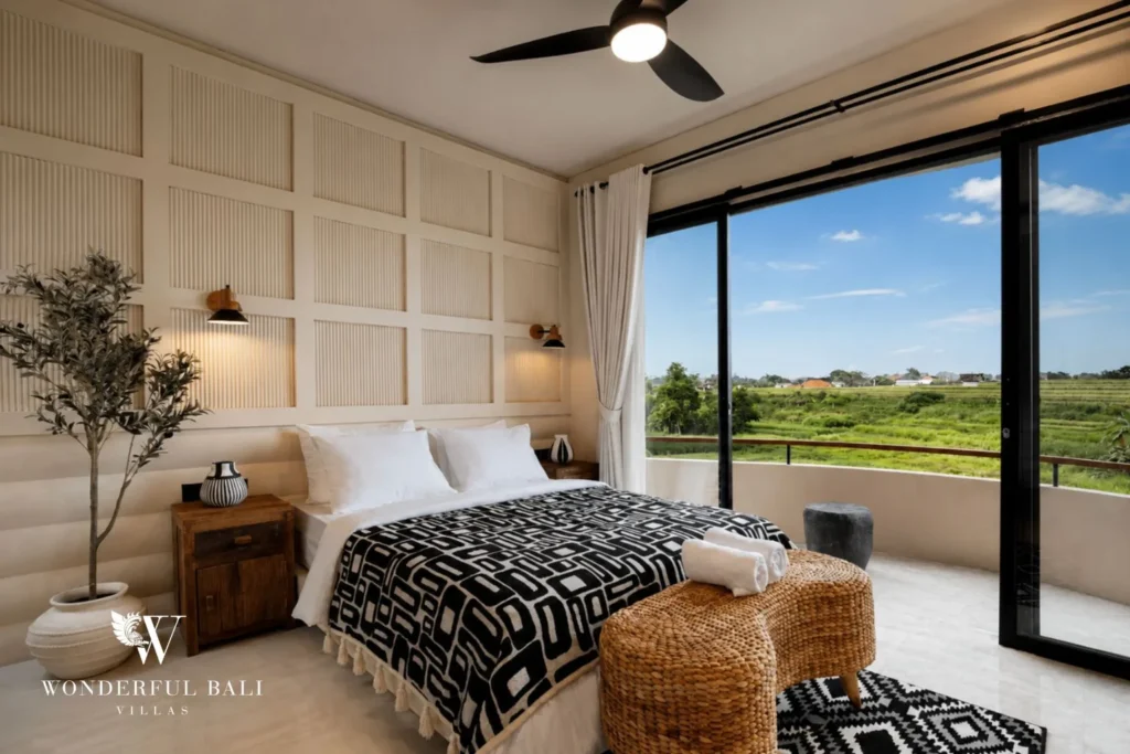 A queen bedroom with patterned bedding and a balcony overlooking green rice fields at a 3-bedroom villa in Pererenan, Bali