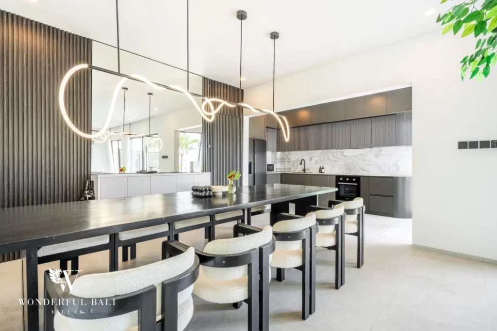 Dining table beneath a sculptural light with the modern kitchen and marble backsplash behind at a 5-bedroom villa in Pererenan, Bali