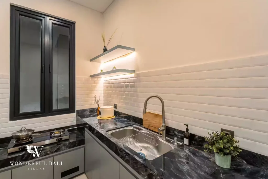 A compact prep kitchen with black marble counters, a gas cooktop, sink and white brick-tiled walls at a 4-bedroom villa in Pererenan, Bali