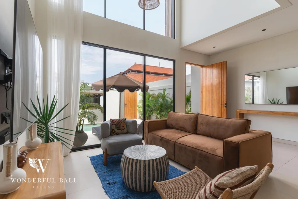 A living room with a brown sofa opening through glass doors to the pool terrace with a parasol at a 2-bedroom villa in Canggu, Bali