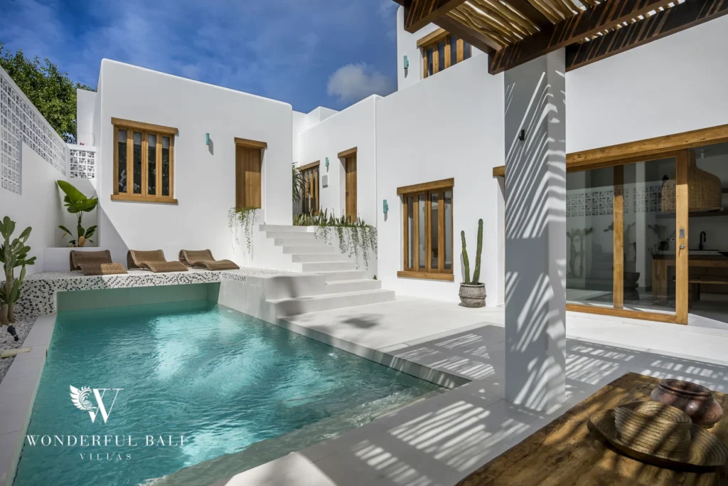 A daytime view of the pool with sun loungers, white steps and cacti wrapping around the whitewashed villa walls and open living pavilion at a 3-bedroom villa in Bingin, Uluwatu, Bali