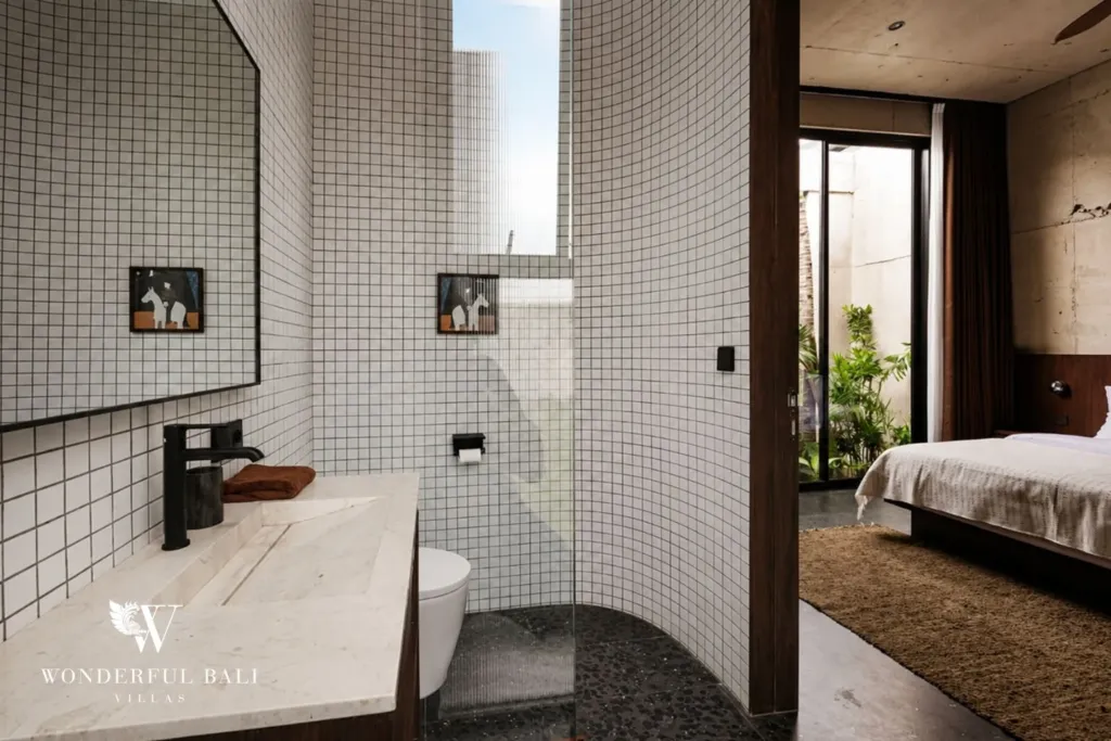 White grid-tiled ensuite with a black faucet, stone vanity and walk-in shower opening to the bedroom beyond at a 2-bedroom villa in Seseh, Bali