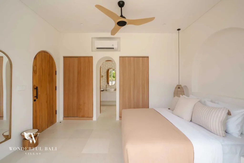 A bedroom with an arched wooden door, timber wardrobes and a view into an ensuite bathroom, at a 2-bedroom villa in Bingin, Uluwatu, Bali
