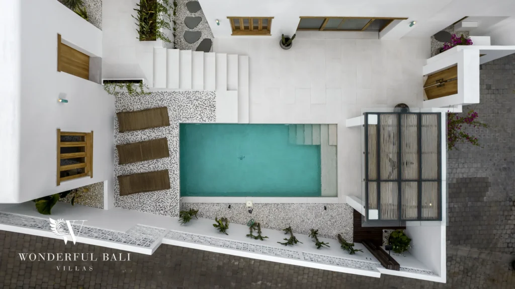 An overhead drone view of the rectangular pool, pebble terraces, staircase and flat white rooftops of the villa surrounded by paving at a 3-bedroom villa in Bingin, Uluwatu, Bali