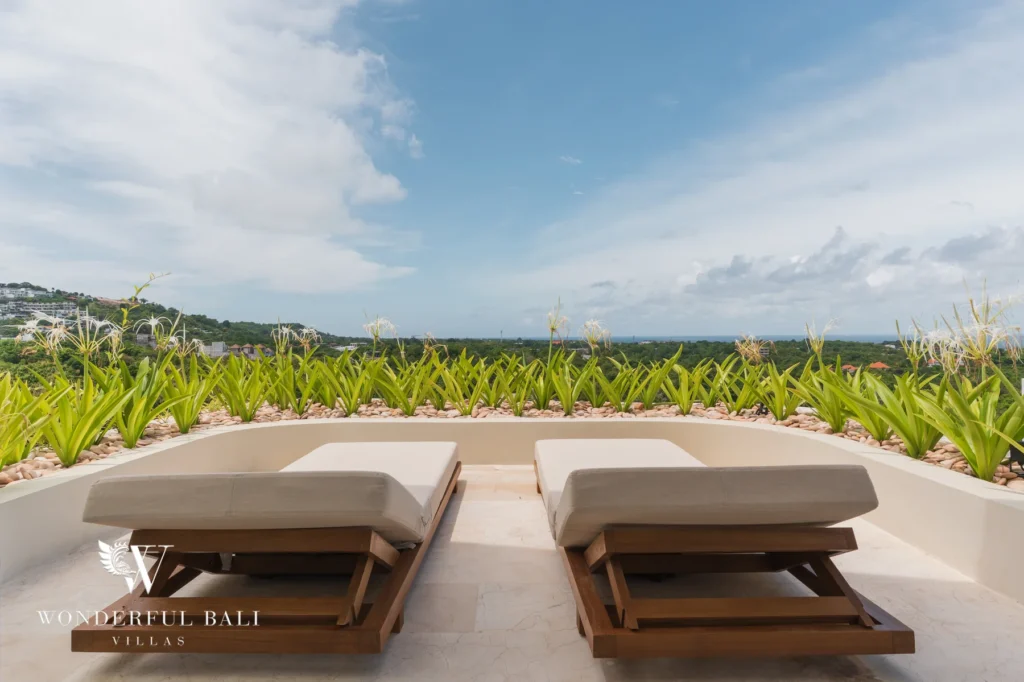 A rooftop terrace with two timber sun loungers set among planting and open panoramic views to the horizon at a 3-bedroom villa in Bingin, Uluwatu, Bali