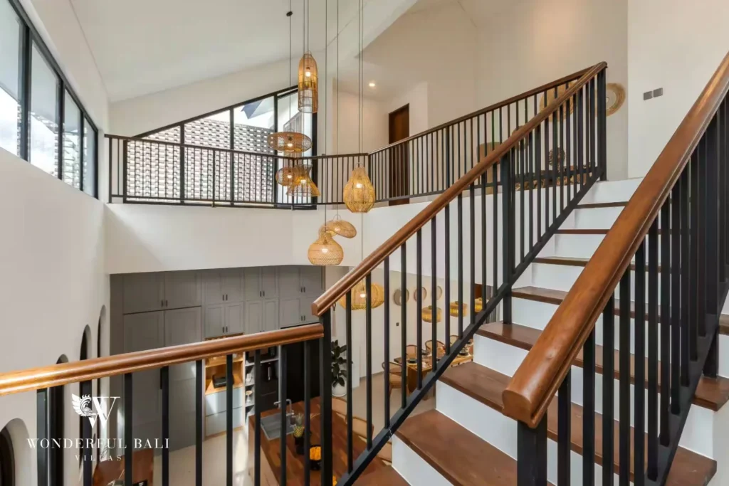 A timber-and-black-steel staircase with woven pendant lights rising through the double-height interior at a 4-bedroom villa in Pererenan, Bali