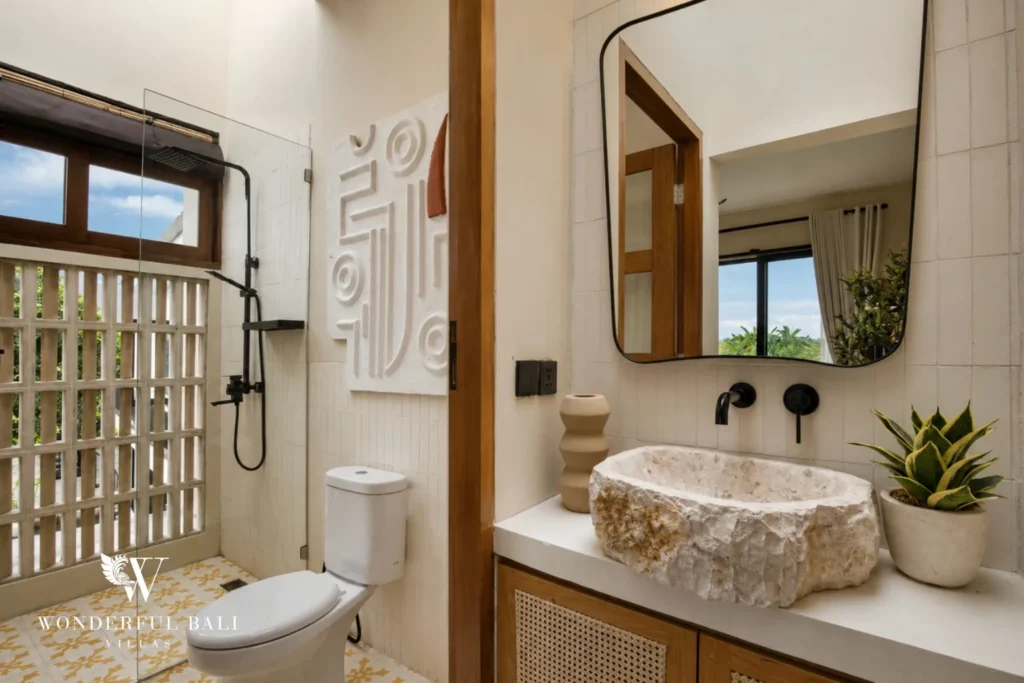An en-suite bathroom with stone basin, glass-block shower and yellow patterned floor at a 3-bedroom villa in Pererenan, Bali
