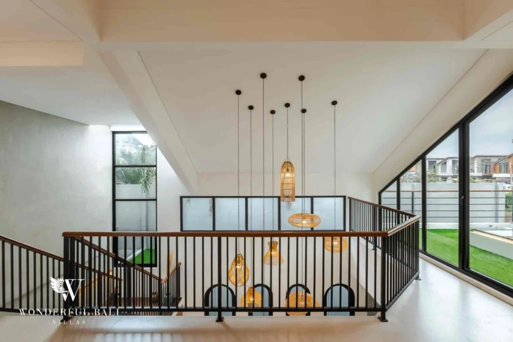 An upstairs landing with a cluster of hanging pendant lights, glass balustrade and views to the garden at a 4-bedroom villa in Pererenan, Bali