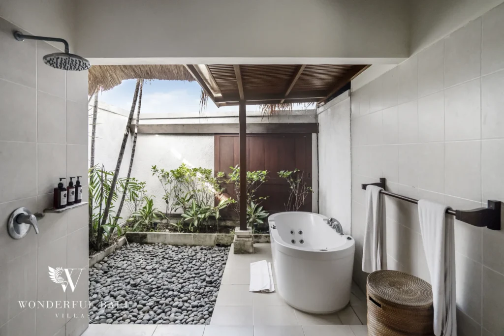 A semi-open bathroom with freestanding tub, rain shower and tropical garden bed of pebble stones at a 4-bedroom villa in Seminyak, Bali