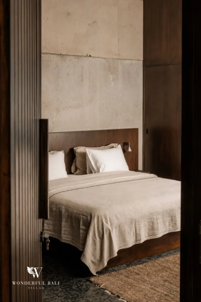 Second bedroom framed by timber, showing a neatly made bed with beige and white linens against a concrete wall at a 2-bedroom villa in Seseh, Bali