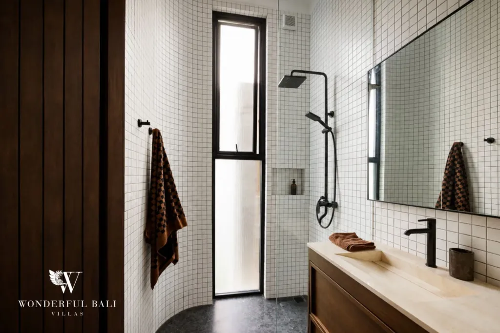 White grid-tiled bathroom with a black rain shower, stone vanity, mirror and a slim frosted window at a 2-bedroom villa in Seseh, Bali