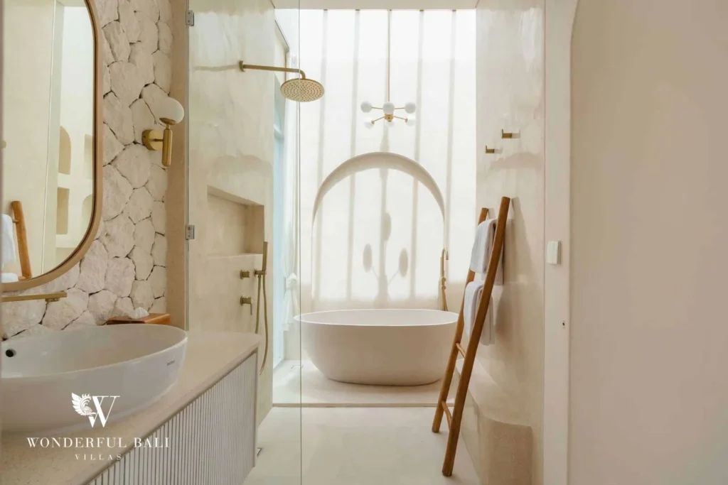 A bathroom with a freestanding tub set in an arched alcove, walk-in shower and a wooden towel ladder, at a 2-bedroom villa in Bingin, Uluwatu, Bali