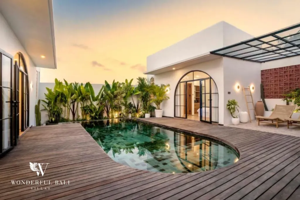 The mosaic-tile pool and wooden deck stretch toward an arched bedroom entry beneath a pastel sunset sky at a 3-bedroom villa in Pererenan, Bali