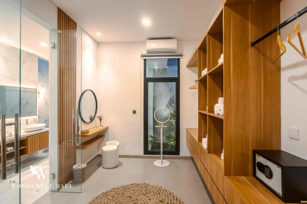A bright dressing area with timber open shelving, a vanity, safe and adjoining marble bathroom at a 4-bedroom villa in Pererenan, Bali
