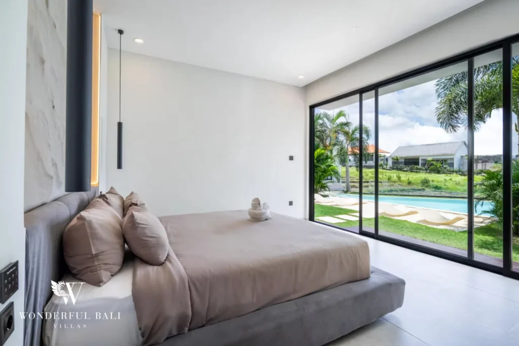King bedroom with a taupe bed and floor-to-ceiling glass doors opening to the pool at a 5-bedroom villa in Pererenan, Bali