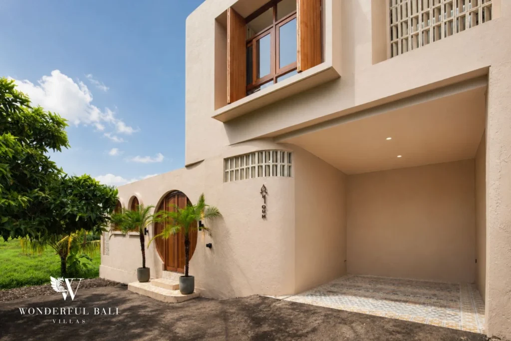 The villa's arched wooden front door and carport under a two-storey facade at a 3-bedroom villa in Pererenan, Bali