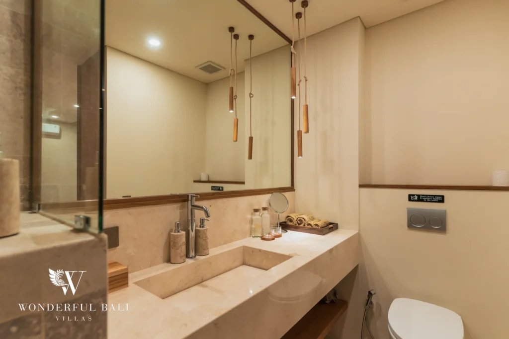 A bathroom with a stone vanity, large framed mirror, pendant lights and a wall-hung toilet at a 3-bedroom villa in Bingin, Uluwatu, Bali