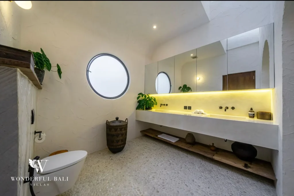 Bathroom with round porthole window pebble floor and lit vanity in a 4-bedroom villa in Canggu Bali