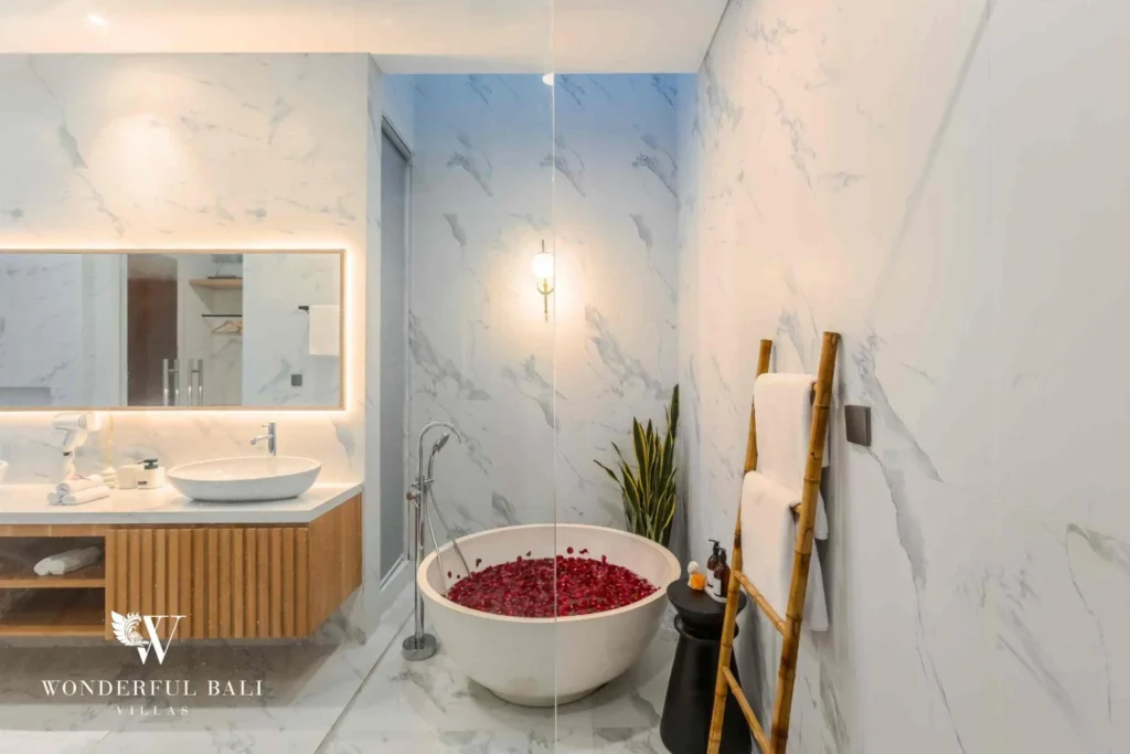A marble bathroom with a round stone soaking tub filled with rose petals beside a floating timber vanity at a 4-bedroom villa in Pererenan, Bali