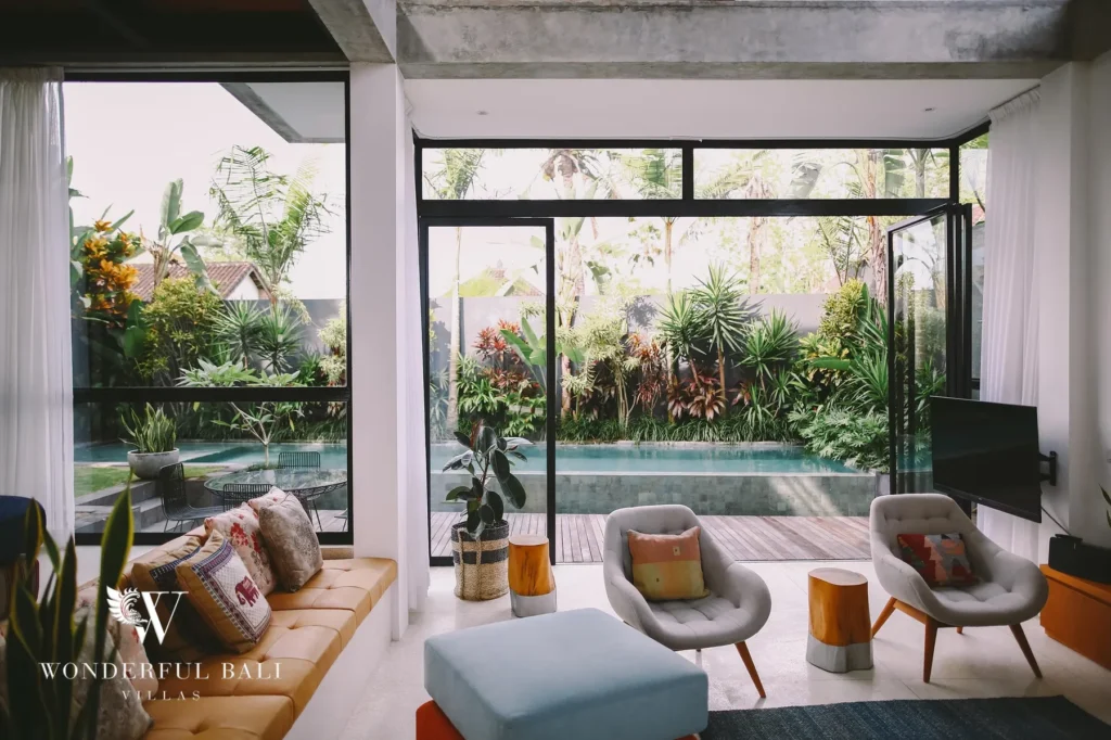 A living area with lounge chairs and retractable glass doors opening fully to the pool and lush tropical garden at a 4-bedroom villa in Batu Bolong, Canggu, Bali