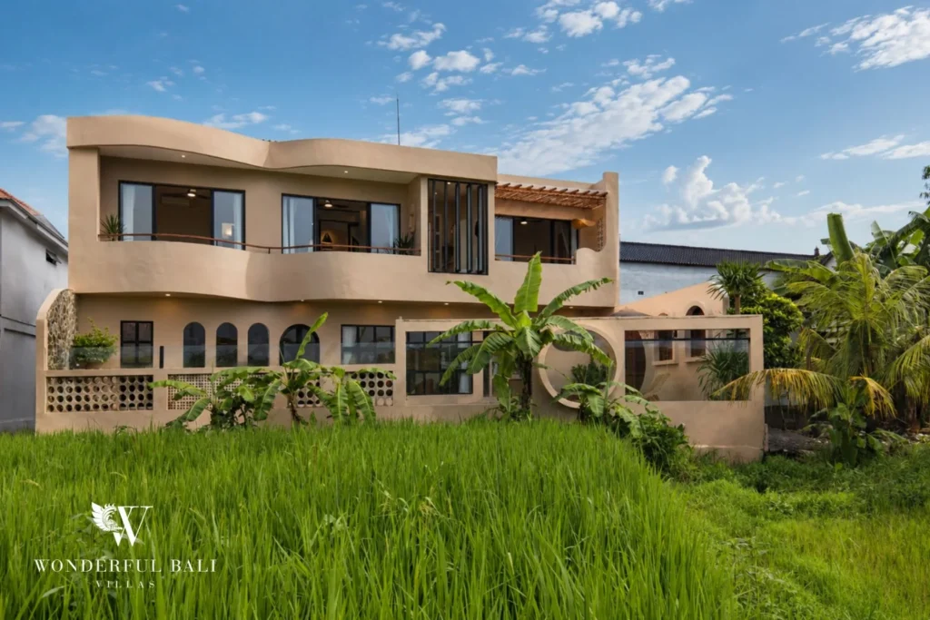 The full two-storey villa facade with balconies rising above lush green rice fields at a 3-bedroom villa in Pererenan, Bali