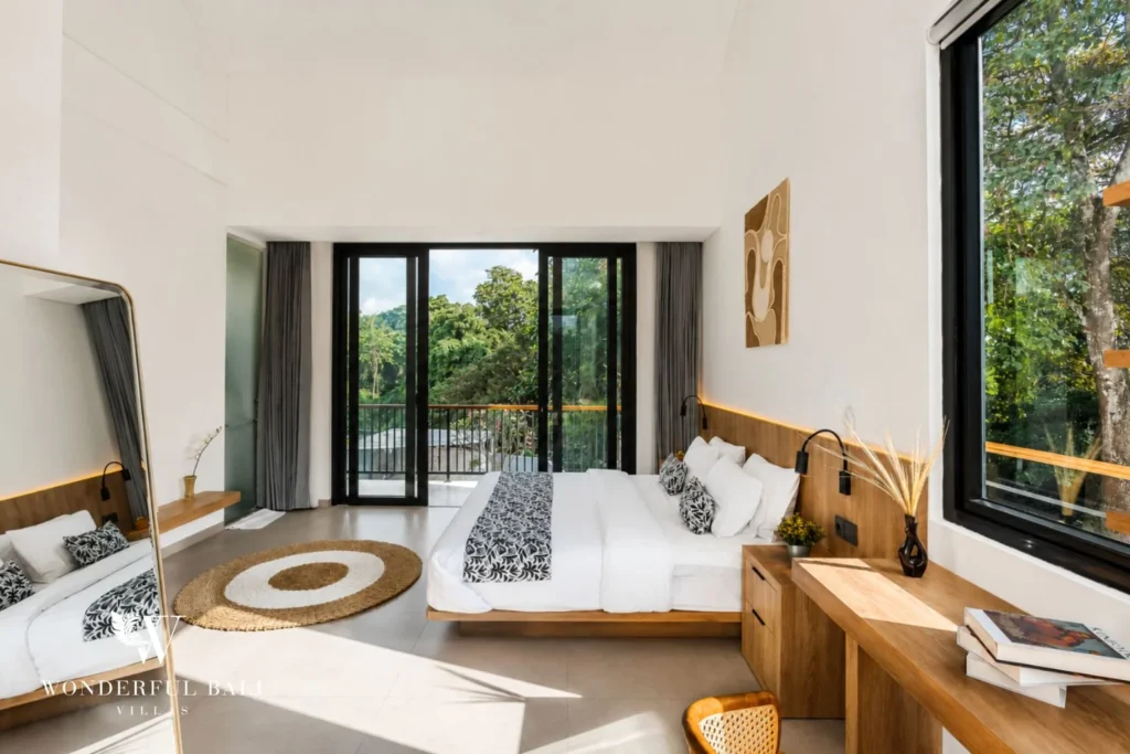 An upstairs king bedroom with high ceilings and sliding doors opening to a balcony over the treetops at a 4-bedroom villa in Pererenan, Bali