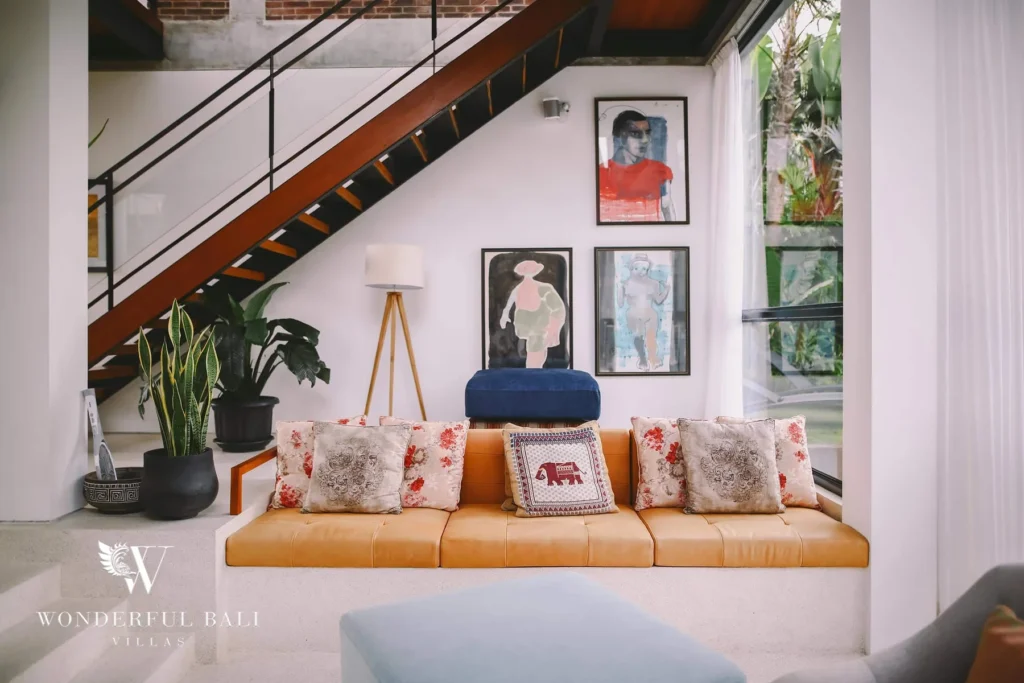 A seating nook beneath the timber staircase with a tan leather sofa, patterned cushions and framed artwork at a 4-bedroom villa in Batu Bolong, Canggu, Bali