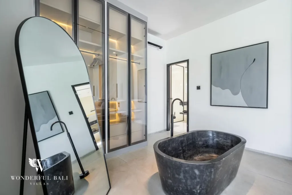 En-suite bathroom with a black stone freestanding tub, arched mirror and glass walk-in wardrobe at a 5-bedroom villa in Pererenan, Bali